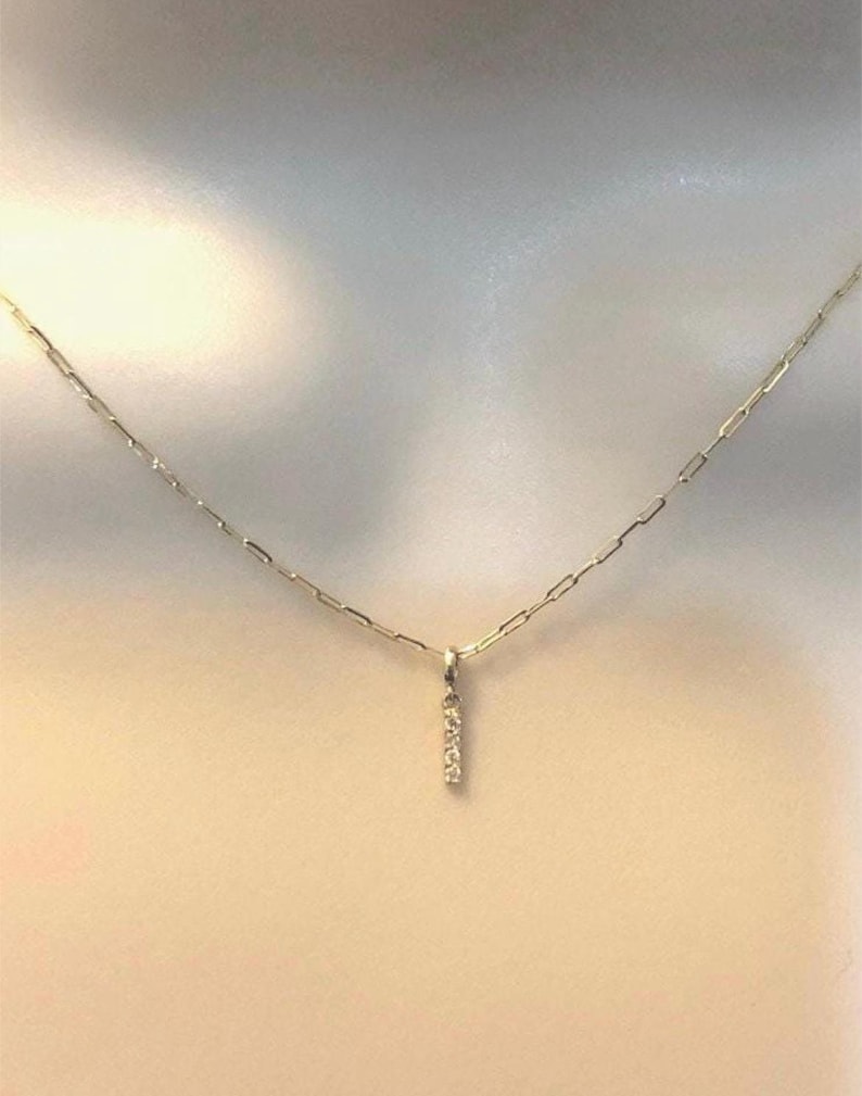 May include: A delicate gold chain necklace with a small pendant featuring a vertical bar of tiny diamonds.