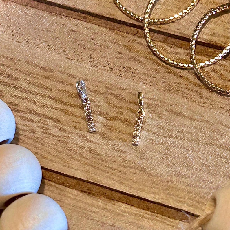 May include: Two gold bar earrings with small clear stones. The earrings are on a wooden surface.