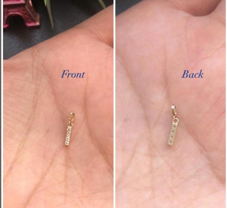 May include: A gold bar charm with small diamonds set into the front. The charm is shown from the front and back.