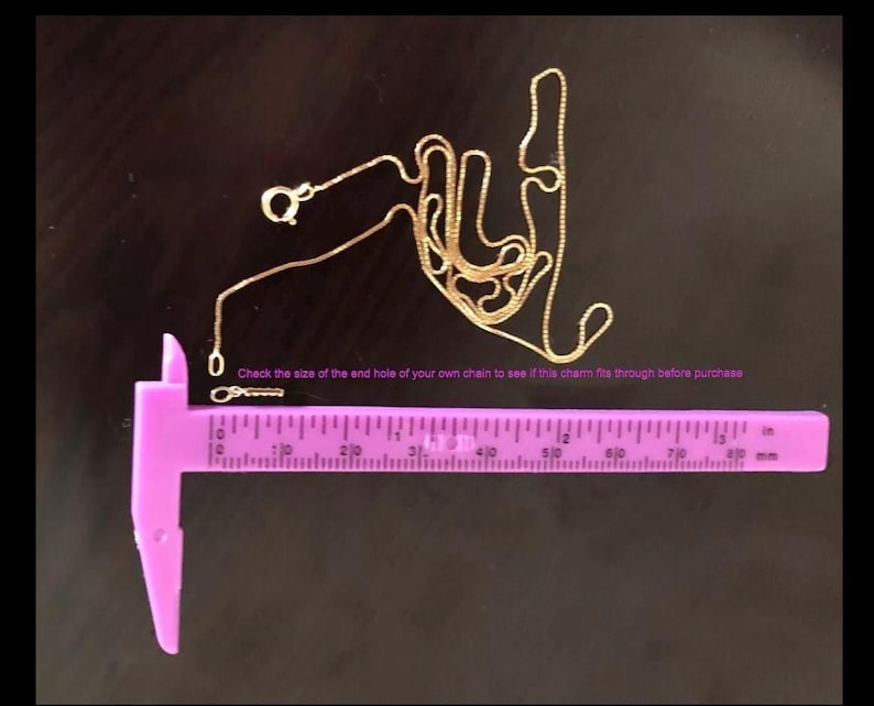 May include: A gold chain with a clasp, measured with a purple ruler. The ruler is marked in inches and millimetres. The text on the ruler reads "Check the size of the end hole of your own chain to see if this charm fits through before purchase."