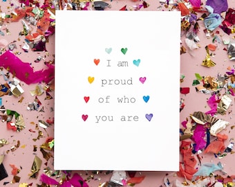 May include: A white card with the text "I am proud of who you are" surrounded by colorful confetti. The text is surrounded by small hearts in various colors.