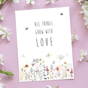 May include: A white card with the text "All things grow with love" in black lettering. The card features a watercolor illustration of a field of wildflowers and butterflies.