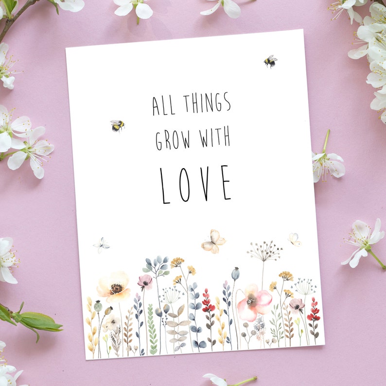 May include: A white card with the text "All things grow with love" in black lettering. The card features a watercolor illustration of a field of wildflowers and butterflies.