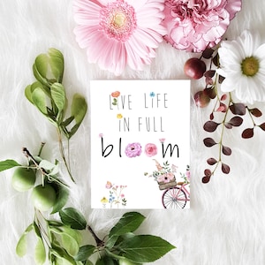 May include: A white card with the text "Live Life in Full Bloom" and a watercolor illustration of a bicycle with a basket full of flowers.