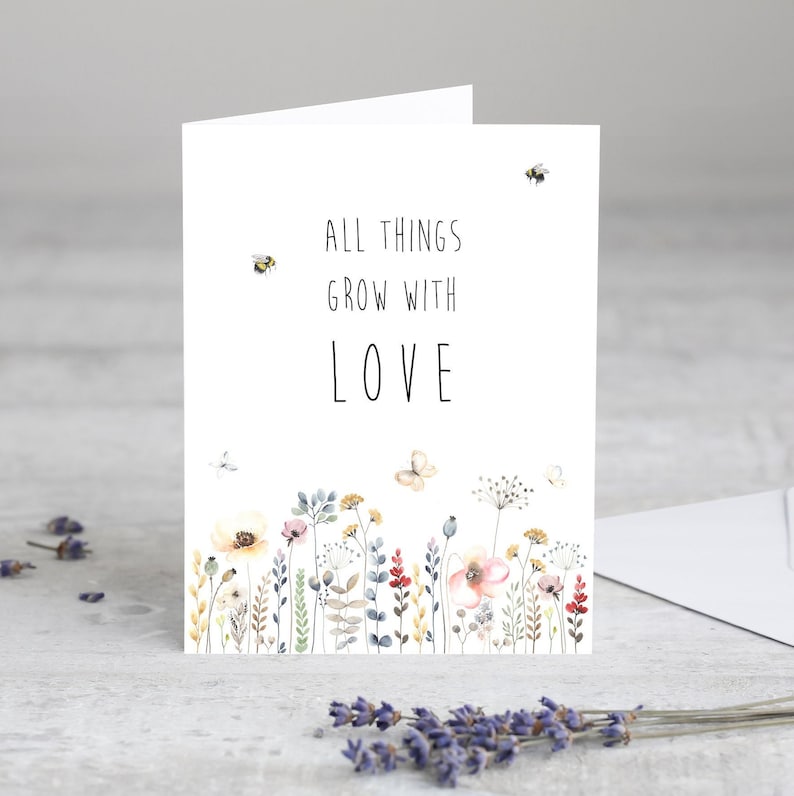 May include: A white card with a watercolor illustration of a field of flowers and bees. The text on the card reads "All things grow with love."