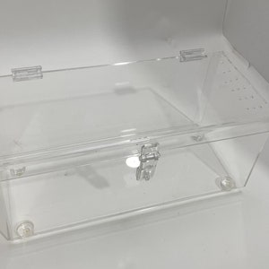May include: A clear acrylic box with a hinged lid and a latch. The box has small holes on the top and sides for ventilation.