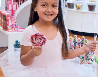 May include: A young girl wearing a pink tutu and a pink shirt holds a colorful lollipop in a candy store.