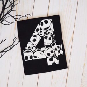 Op de afbeelding: Zwart T-shirt met een wit nummer vier gemaakt van het gezicht van Jack Skellington uit de film The Nightmare Before Christmas.