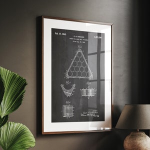 Könnte beinhalten: Ein gerahmter Schwarzweißdruck einer Patentzeichnung für einen Billardkugel-Dreiecksständer. Das Patent trägt den Titel "Billiard Ball Triangle Rack" und wurde am 17. Februar 1942 von C.M. Weicker eingereicht. Die Patentnummer lautet 2,373,338.