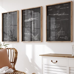 Może przedstawiać: Trzy oprawione czarno-białe vintage wydruki wzorów łodzi z tekstem "E.P. Davis Row Boat" i "Patented Aug. 1, 1905" na prawym wydruku. Wydruki wiszą na białej ścianie nad białą szafką z drewnianym blatem. W pierwszym planie znajduje się wiklinowe krzesło z brązową poduszką i białym kocem.