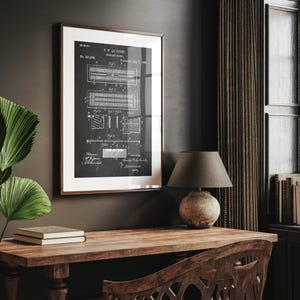 Op de afbeelding: Een ingelijste zwart-wit afdruk van een patentdiagram hangt aan een donkere muur. Het diagram, getiteld "C.W. Le Count", toont gedetailleerde technische tekeningen. Een houten bureau met een lamp en boeken staat onder de afdruk.