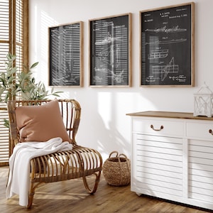 Puede incluir: Tres impresiones de patentes en blanco y negro enmarcadas en marcos de madera cuelgan de una pared blanca. Una silla de mimbre con un cojín melocotón y una manta blanca está frente a una ventana. Un mueble blanco y una cesta tejida también están en la habitación.