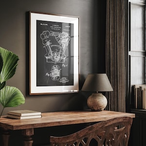 May include: Framed black and white blueprint of an engine, dated May 16, 1944. The print is in a brown frame with a white mat. The image is displayed on a wooden desk with a lamp and books.