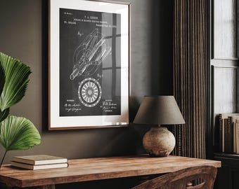 Op de afbeelding: Een ingelijste zwart-wit print van een T.A. Edison patent voor een dynamo elektrische machine. De print wordt weergegeven op een houten bureau met een lamp en boeken. De print heeft een witte rand en een donkerbruine lijst.