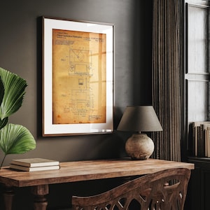 May include: Framed patent print of a handheld gaming device, with detailed technical drawings. The print has a vintage aesthetic with a brown and beige colour scheme. The frame is a dark brown colour, and the print is displayed on a wooden desk.
