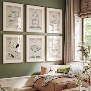 May include: Six framed vintage video game console patent prints. Each print features a detailed black and white technical drawing of a console, set against a cream-colored background. The frames are a warm gold color, and the prints are displayed on a green wall.