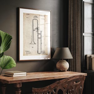 Puede incluir: Impresión enmarcada de patente de trombón vintage. La obra de arte presenta una ilustración detallada en blanco y negro de un trombón sobre papel envejecido, enmarcada en un marco de madera marrón. La impresión se exhibe en una pared oscura, encima de un escritorio de madera.