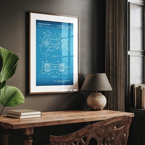 May include: Framed blueprint of a video game controller, featuring detailed diagrams of the device's components. The artwork is set against a blue grid background, with the text "United States Patent" at the top. The frame is brown.