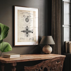 May include: A framed vintage print of a Tesla patent for an alternating current dynamo electric generator. The print is in a dark wooden frame and hangs on a dark wall. The print has a sepia tone and is displayed above a wooden desk.