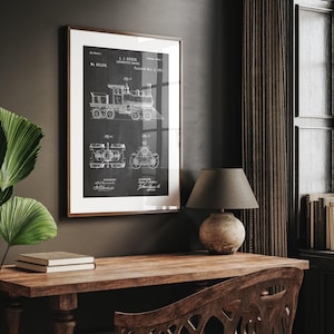 May include: A framed black and white print of a locomotive engine patent. The print, with the text "A.J. Huber Locomotive Engine," is in a brown frame. The image is above a wooden desk with a lamp and books, creating a vintage aesthetic.