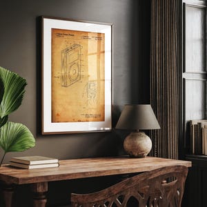 May include: Framed patent print of a portable media player, featuring detailed technical drawings on aged paper. The print is encased in a brown frame with a white mat, suitable for home or office decor. The patent number is visible.
