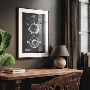 May include: Framed black and white print of a teapot patent design. The artwork features detailed technical drawings of a teapot and its components, with text and diagrams. The frame is a warm brown color, and the print is displayed on a dark wall.