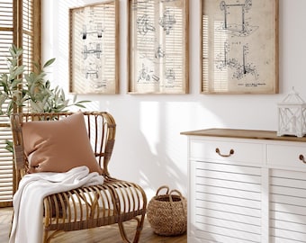 Op de afbeelding: Drie ingelijste vintage patentprints van gewichthefapparatuur hangen aan een witte muur. De prints zijn in houten frames en tonen gedetailleerde technische tekeningen. Een rieten stoel met een perzikkleurig kussen en een witte deken staat onder de prints.