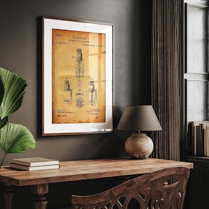 May include: Framed vintage patent print of an automatic fire sprinkler. The print features detailed technical drawings and text on aged paper, set within a brown frame. The print is displayed on a wooden desk with a lamp and books.