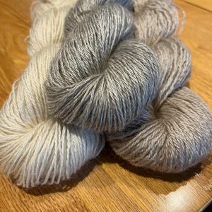 May include: Three skeins of yarn in different shades of gray and white. The yarn is soft and fluffy, and it is perfect for knitting or crocheting.