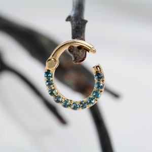 May include: Gold hoop earring with a row of blue gemstones around the edge.