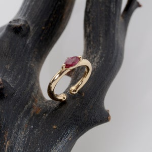 May include: A gold ear cuff with a single red gemstone. The cuff is open and has a rounded end.