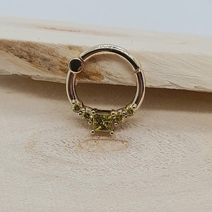 May include: A gold circular ring with a row of small green gemstones and a larger square green gemstone in the center.