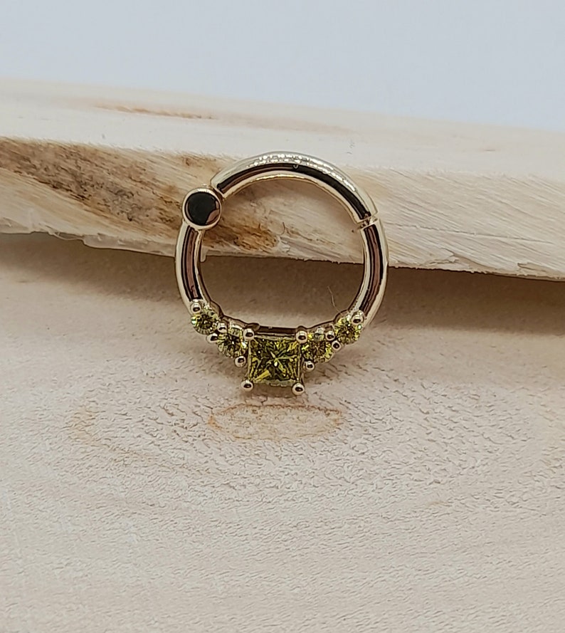 May include: A gold circular ring with a row of small green gemstones and a larger square green gemstone in the center.