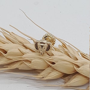 May include: Gold elephant stud earring with a textured surface. The earring is on a background of wheat stalks.