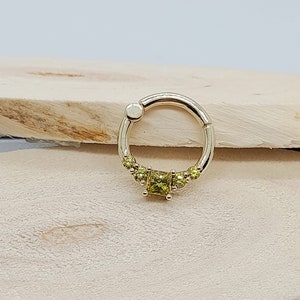 May include: A gold ring with a square-shaped green gemstone in the center and smaller green gemstones surrounding it.