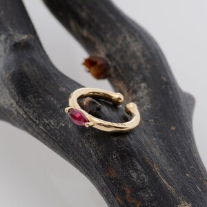 May include: A gold ear cuff with a single red gemstone. The cuff is open and has a simple design.