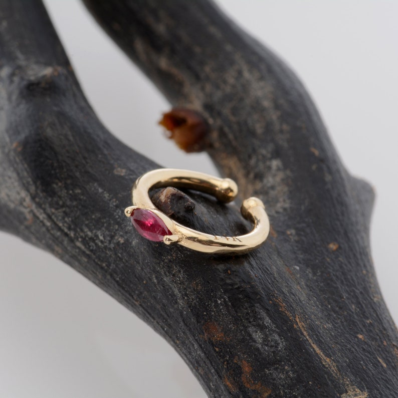 May include: A gold ear cuff with a single red gemstone. The cuff is open and has a simple design.