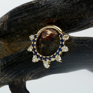 May include: A gold hoop earring with a row of blue gemstones and a row of clear gemstones around the hoop.
