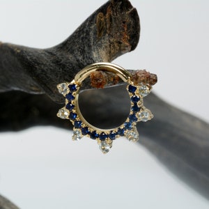 May include: A gold hoop earring with a row of blue gemstones and a row of clear gemstones around the hoop.
