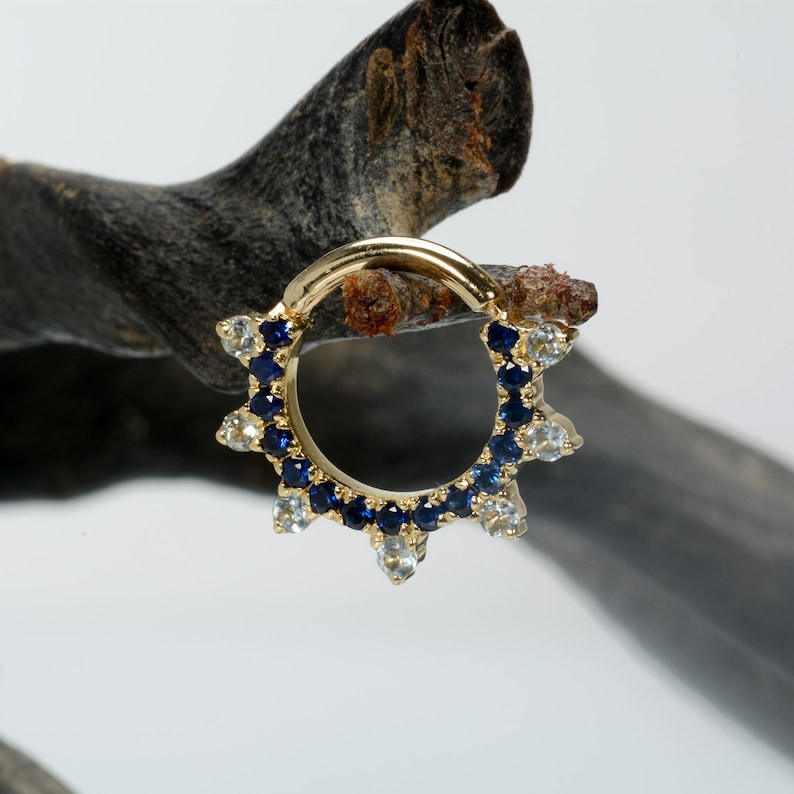 May include: A gold hoop earring with a row of blue gemstones and a row of clear gemstones around the hoop.