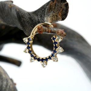 May include: A gold hoop earring with a row of blue gemstones and a row of clear gemstones around the hoop.