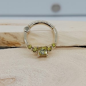 May include: A gold hoop earring with a single square-shaped yellow gemstone surrounded by smaller yellow gemstones