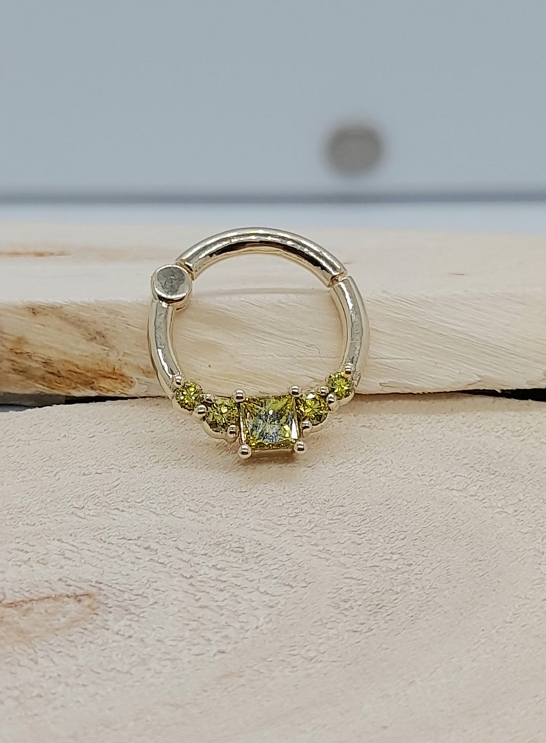 May include: A gold hoop earring with a single square-shaped yellow gemstone surrounded by smaller yellow gemstones