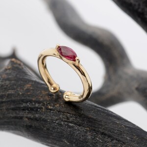 May include: A gold ear cuff with a single red gemstone. The ear cuff is a simple design with a smooth finish.