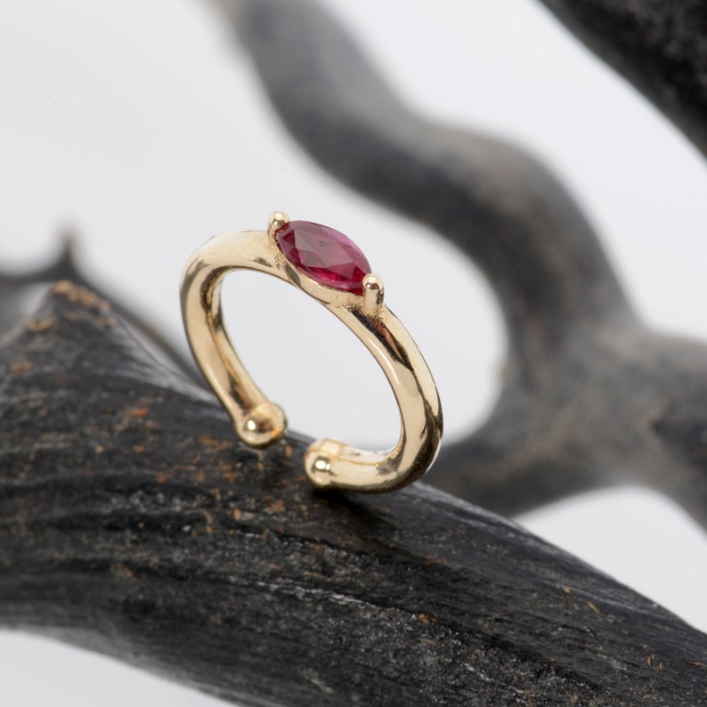 May include: A gold ear cuff with a single red gemstone. The ear cuff is a simple design with a smooth finish.