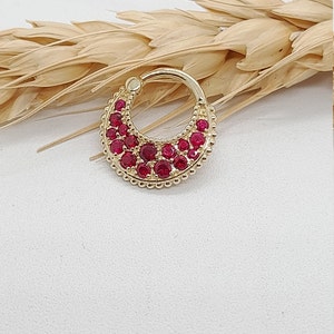 May include: Gold hoop earring with a crescent moon design set with red gemstones.