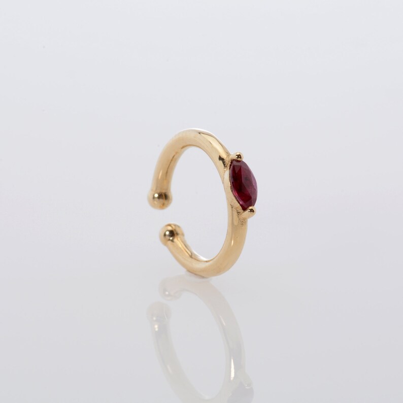 May include: Gold ear cuff with a single red gemstone.