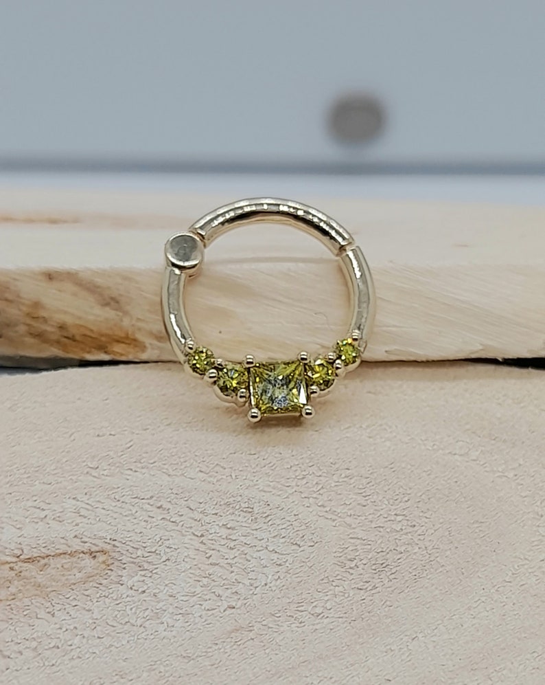 May include: A gold ring with a square-shaped yellow gemstone in the center. The ring is decorated with smaller yellow gemstones on either side of the center stone.