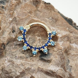 May include: A gold septum ring with a blue and light blue crystal halo