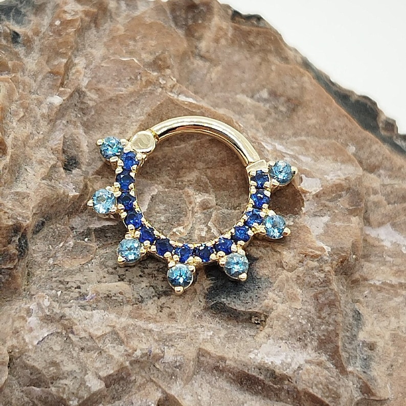 May include: A gold septum ring with a blue and light blue crystal halo